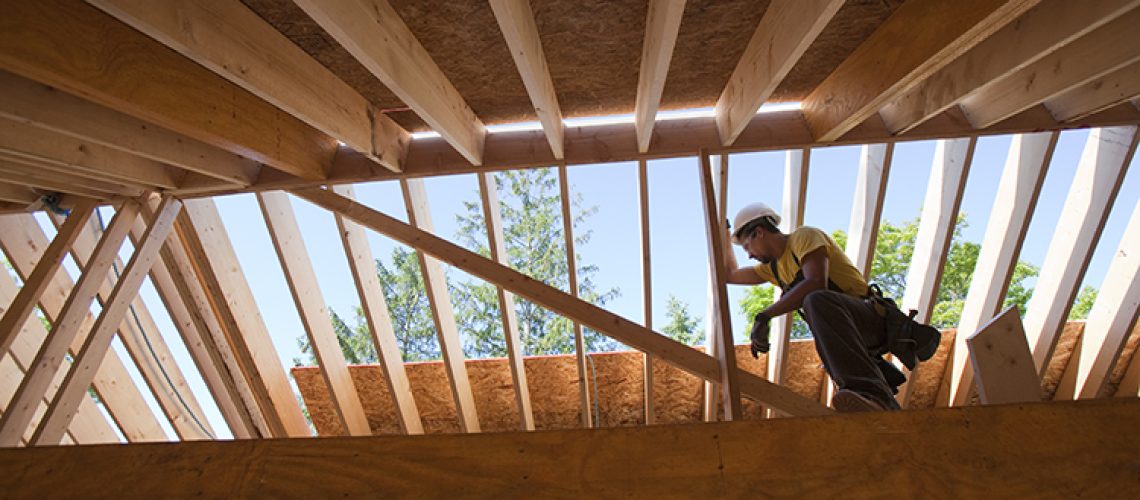 carpenter with a circular saw on rafter at a house under construction